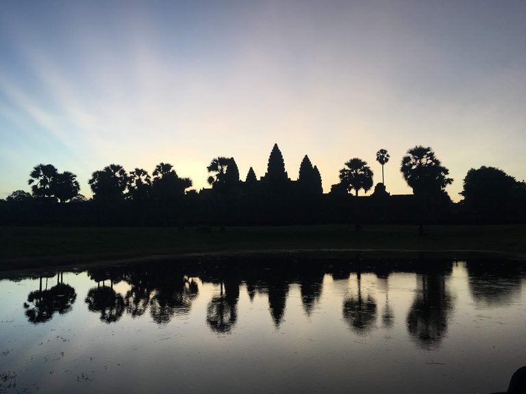 Angkor Wat's five towers silhouetted at dawn, mirrored in the still reflecting pool.