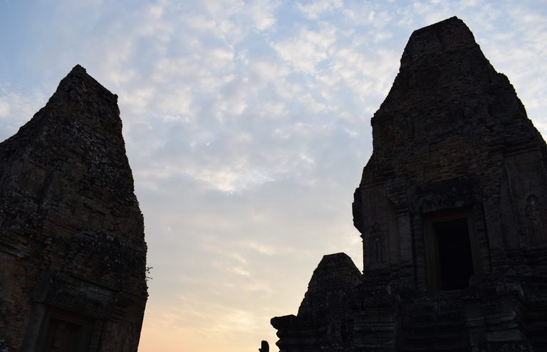 Pre Rup's brick temple towers silhouetted against a soft golden sunset sky.