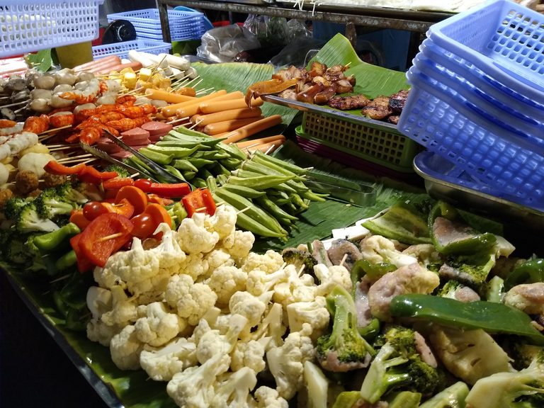 A night-market stall spread with skewers, meats and vegetables ready for the grill.