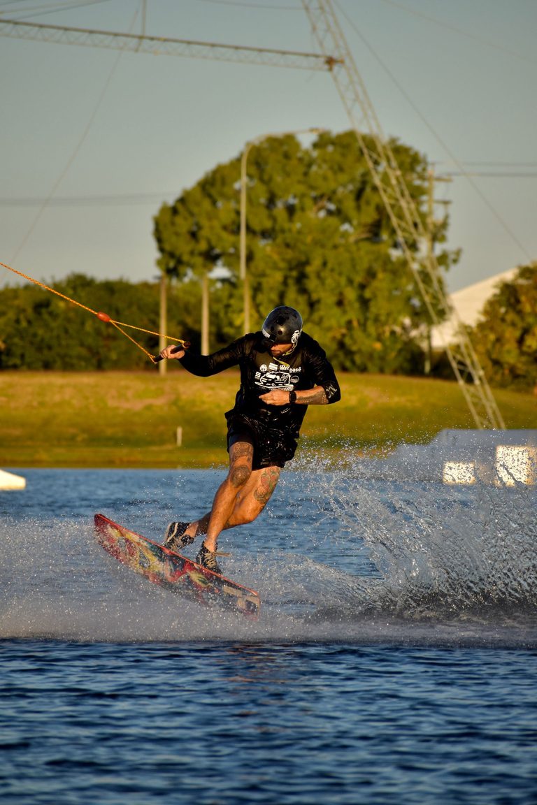 A wakeboarder throws up spray mid-jump on a cable-park lake at golden hour.
